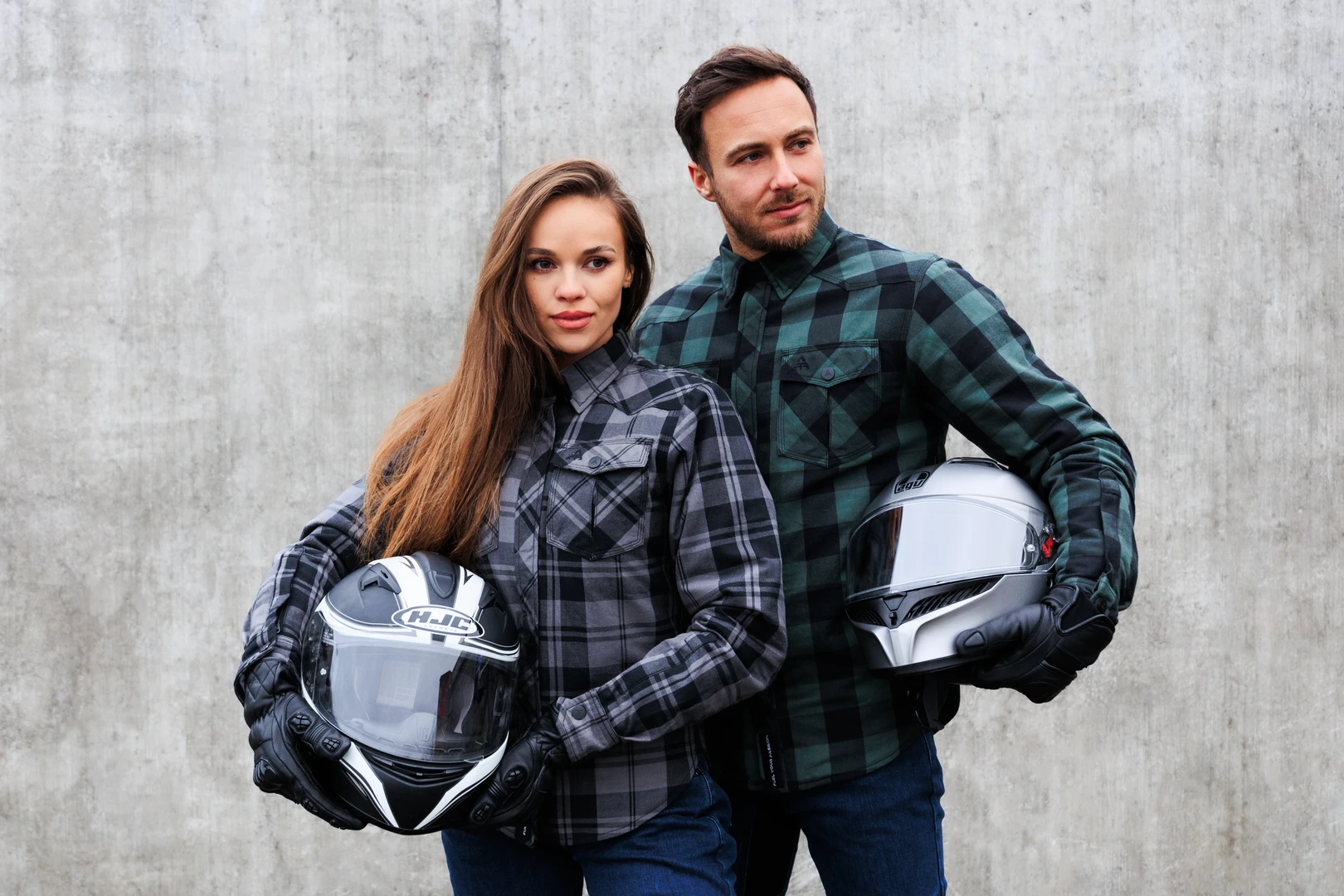 Alfa Thrust – odzież motocyklowa, kobieta i mężczyzna w kurtkach motocyklowych z kaskami pod pachą na szarym tle.
