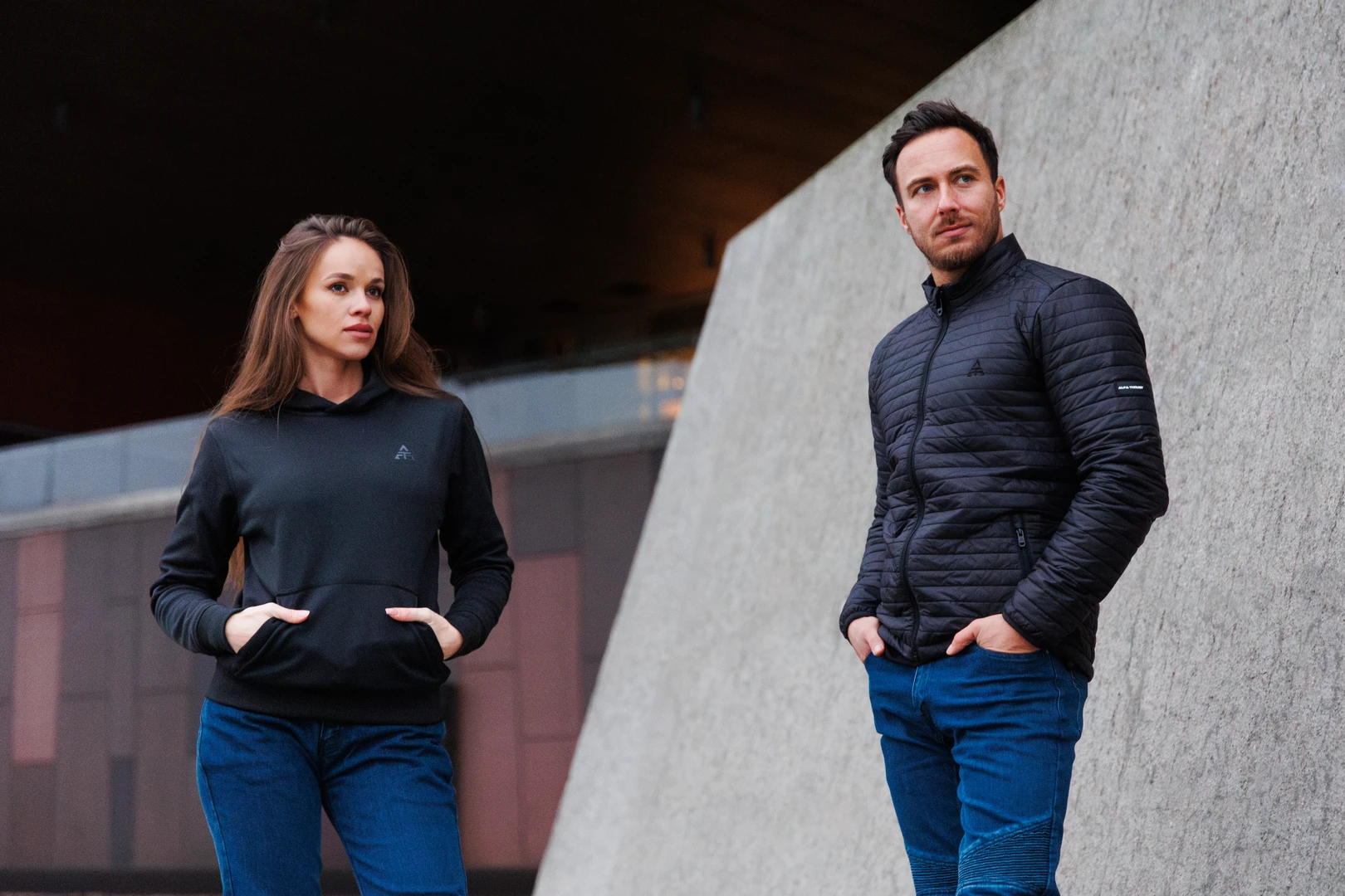 Alfa Thrust – odzież motocyklowa, kobieta i mężczyzna w czarnych kurtkach i jeansach motocyklowych na miejskim tle.