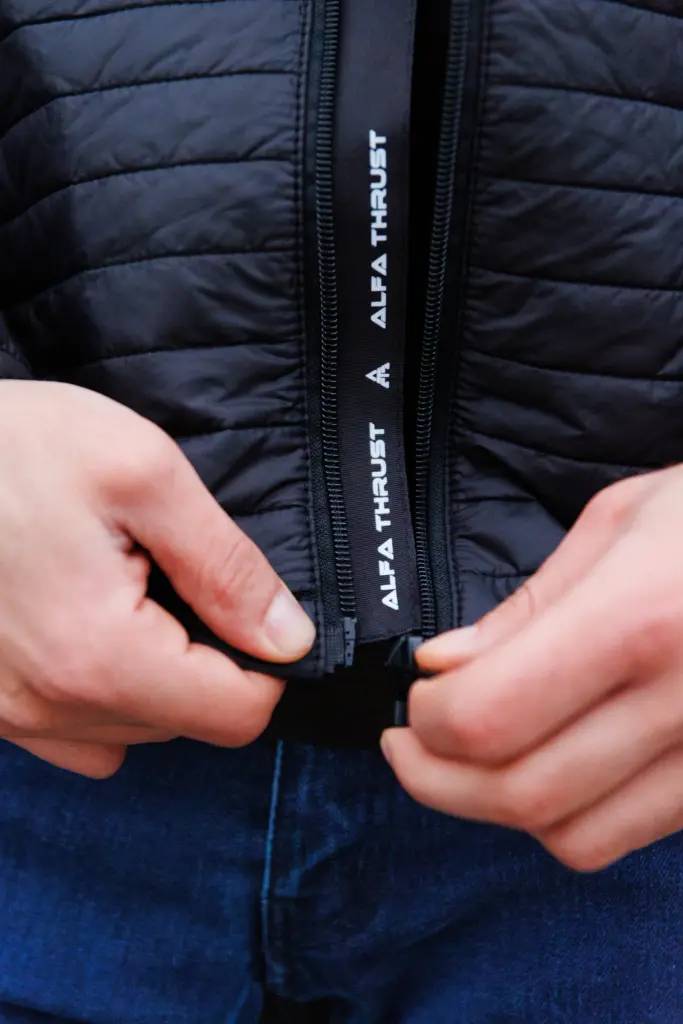 Kurtka motocyklowa – odzież motocyklowa, zbliżenie na dłonie zapinające zamek błyskawiczny w czarnej kurtce pikowanej.