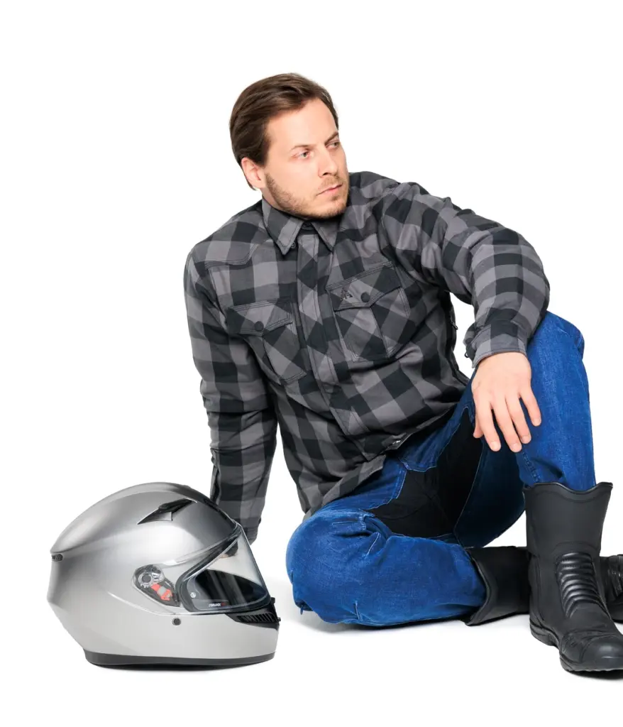 Alfa Thrust Erick Storm – spodnie motocyklowe, mężczyzna w jeansach i koszuli siedzący obok kasku na białym tle.